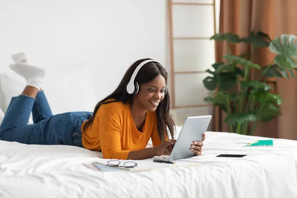 アフリカ系アメリカ人女性がベッドルームでヘッドフォンを着用してデジタルタブレットを使用 — ストック写真