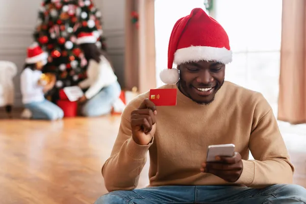 Xmas Online Shopping. Svart man med mobiltelefon som visar kreditkort — Stockfoto