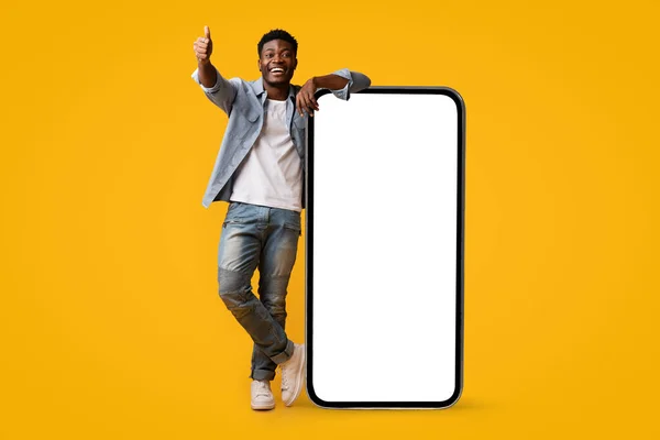 Glada svart man står vid enorm mobiltelefon, mockup — Stockfoto