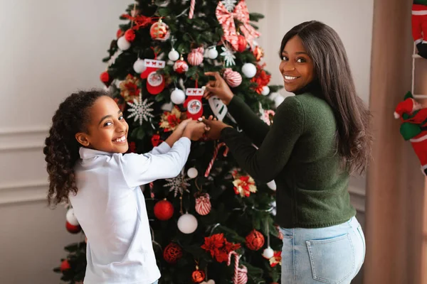 Mulher negra feliz e menina decoração árvore de Natal, olhando para trás — Fotografia de Stock