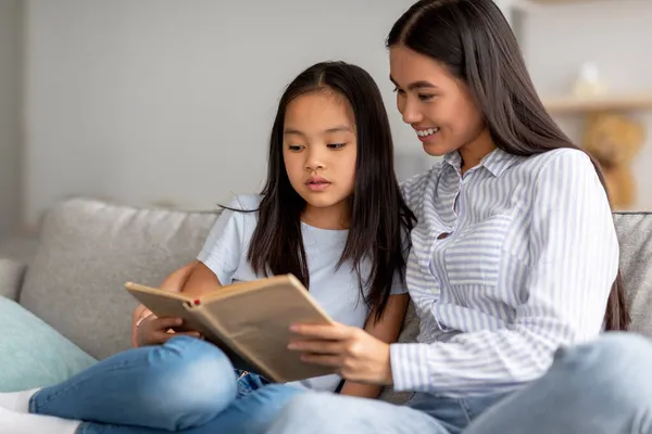 Familie tijdverdrijf. gelukkig aziatische moeder en haar dochter lezen boek samen, tijd doorbrengen thuis, vrije ruimte — Stockfoto