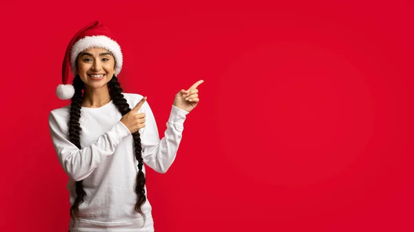 Vánoční reklama. Šťastný mladý Arab žena v santa klobouk ukazující ven — Stock fotografie