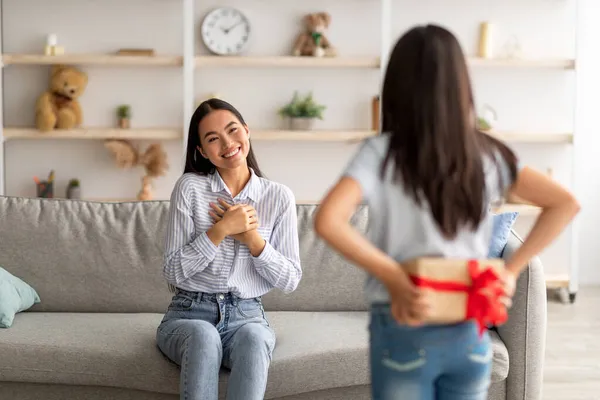 Celebración del Día de las Madres. Chica ocultando caja de regalo detrás de su espalda, felicitando sorprendida madre asiática con vacaciones — Foto de Stock