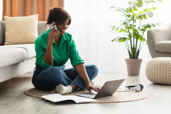 Afrikanska kvinnliga pratar på mobiltelefon med bärbar dator hemma — Stockfoto