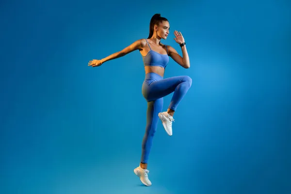 Athletin beim Springen während des Trainings vor blauem Studiohintergrund — Stockfoto