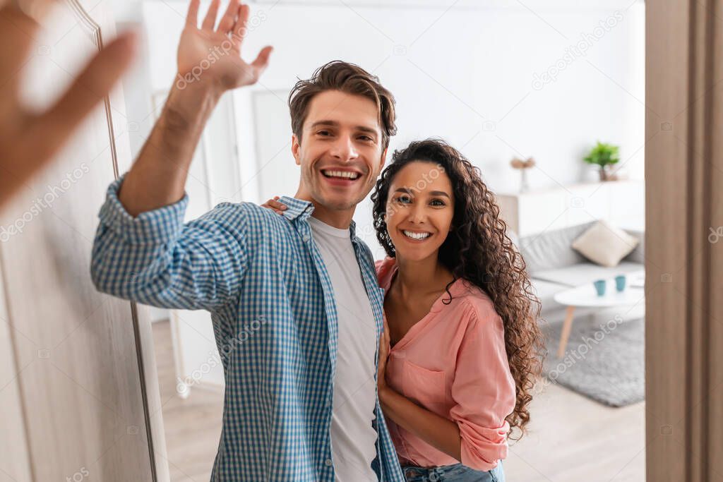 Happy couple inviting people to enter home, giving high five