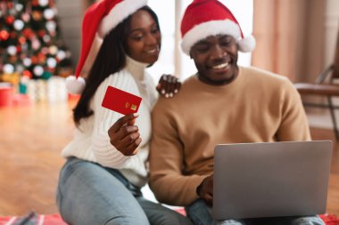 Gülümseyen siyah çift Xmas 'ta kredi kartını gösteren bir dizüstü bilgisayar kullanıyor.