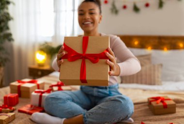 Noel hediyesi konsepti. Heyecanlı Afrikalı Amerikalı kadın hediye kutusunu kameraya uzatıyor ve gülümsüyor, seçici odaklanıyor.