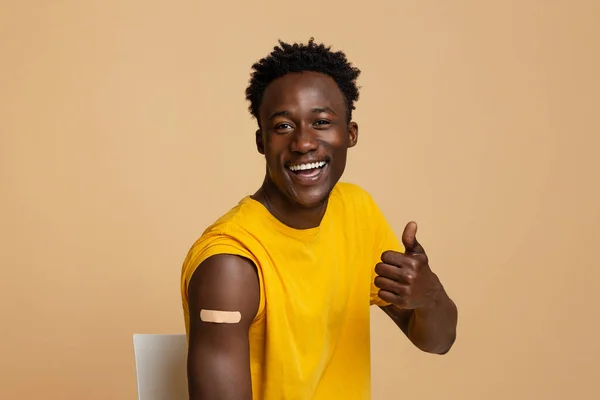 Campaña de vacunación. Feliz hombre negro mostrando el pulgar hacia arriba después de recibir la vacuna —  Fotos de Stock