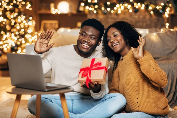 Xmasのギフトボックスを持つ陽気な黒のカップルは、ラップトップ上でビデオ通話を作る、自宅からクリスマスオンラインで友人を迎える — ストック写真