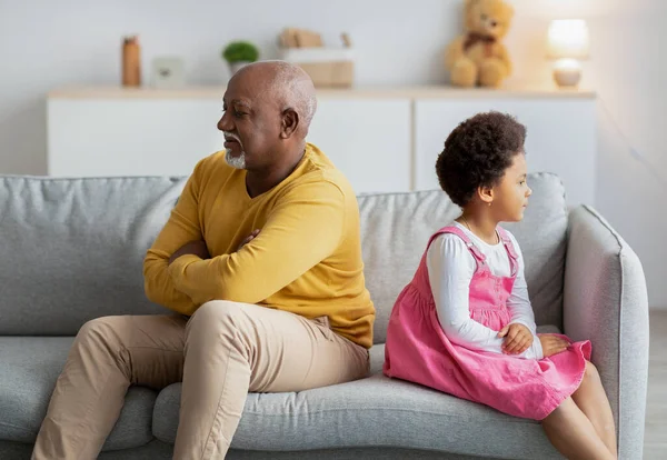 Ofendido afro-americano criança pequena e homem maduro ignorar uns aos outros após briga no sofá na sala de estar — Fotografia de Stock