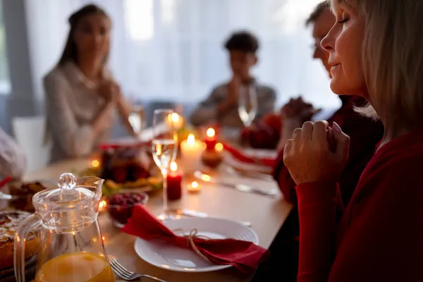 Idős hölgy és a tágabb család imádkozik, hálát adva Istennek, asztalnál ülve ünnepi étellel otthon — Stock Fotó