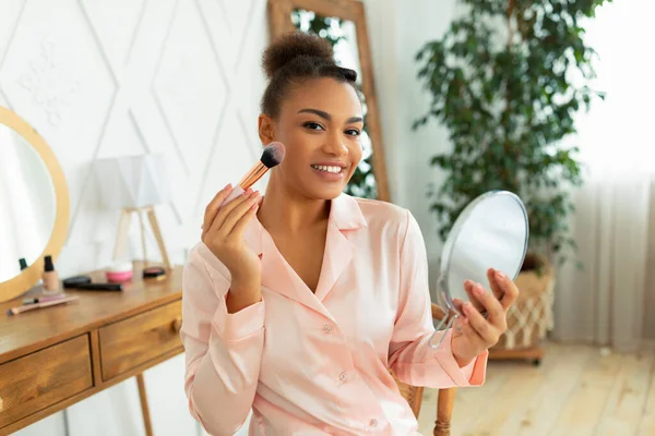 Rotinas de beleza e maquiagem. Feliz senhora afro-americana aplicando blusher, segurando espelho e sorrindo para a câmera — Fotografia de Stock