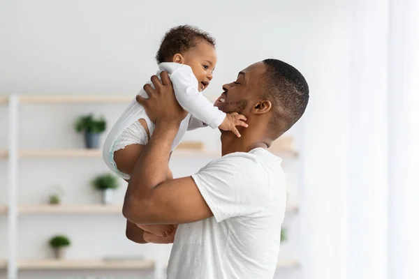 Vatertagskonzept. Liebender junger schwarzer Papa, der süße Säuglinge hochhebt — Stockfoto