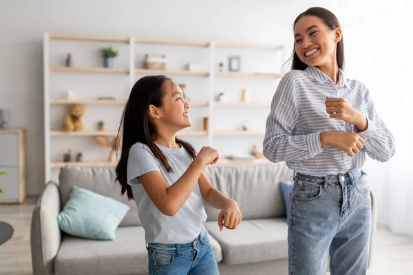 Emocionado mamá asiática y linda hija bailando con música y divirtiéndose en casa, sonriendo el uno al otro — Foto de Stock