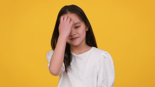 Kleines Modelabel. Liebenswert preteen asiatische Mädchen posiert und lächelt vor der Kamera, spielt mit ihren Haaren, orange Hintergrund — Stockvideo