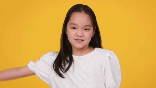 面白い小さなアジアの女の子ショー二足,小さな筋肉を示す,笑顔でカメラにオレンジのスタジオの背景 — ストック動画