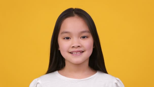 Primer plano estudio retrato de adorable bastante preadolescente asiático chica sonriendo a cámara, posando sobre naranja estudio fondo — Vídeos de Stock