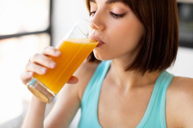 Sağlıklı beslenme ve detoks konsepti. Genç bayan bardaktan taze portakal suyu içiyor, lezzetli meyve suyunun tadını çıkarıyor.
