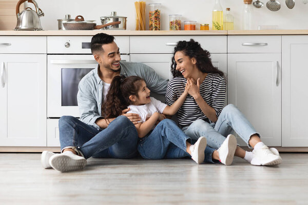 Beautiful middle eastern family sitting on floor at kitchen