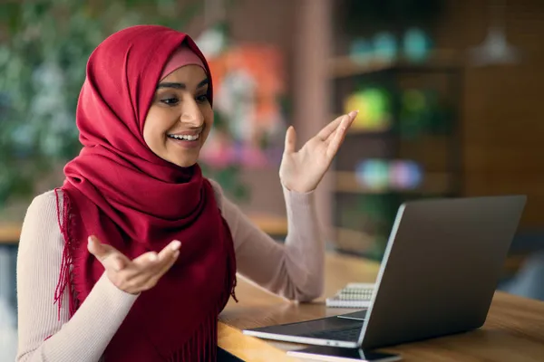 ヒジャーブ州の陽気なイスラム教徒の女性は、ラップトップを使用してビデオチャットを持っています — ストック写真
