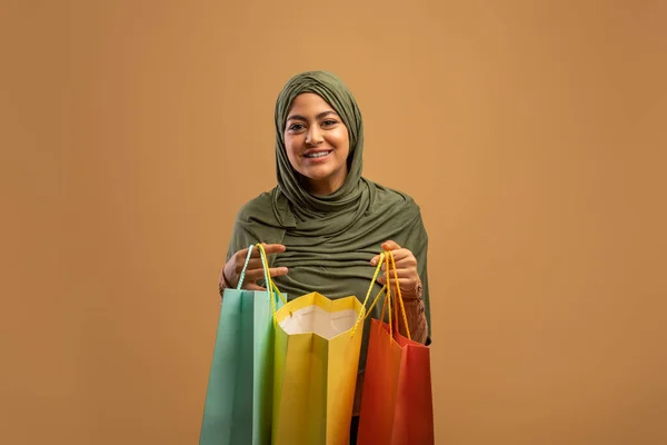 満足した顧客。興奮アラブ女性オープンカラフルなショッピングバッグと笑顔でカメラ、茶色の背景、バナー — ストック写真