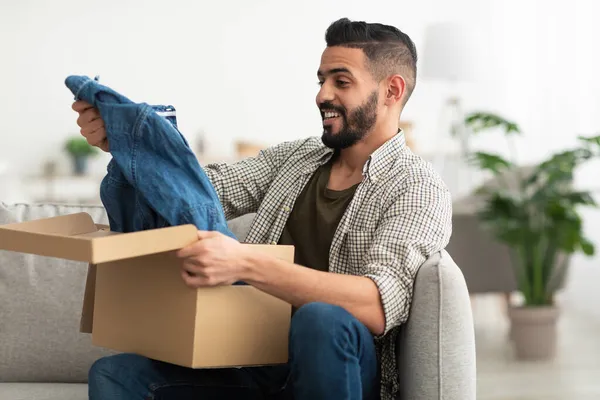 Heureux homme arabe sortir de nouveaux vêtements de la boîte en carton, satisfait du service de livraison à la maison — Photo