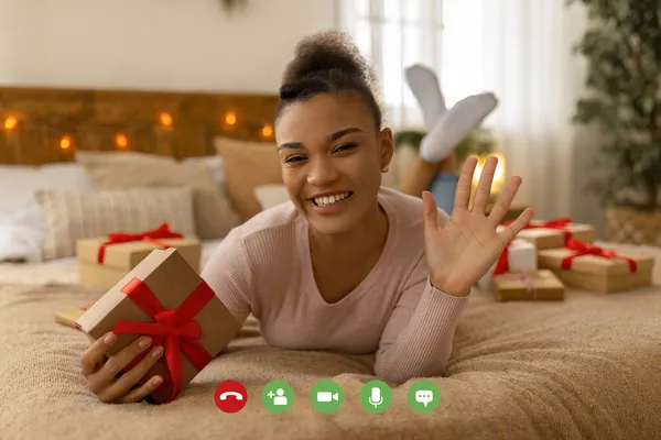 Wirtualne świąteczne pozdrowienia. Monitor widok szczęśliwy czarny lady gospodarstwa obecny polu i machając ręką do laptopa ekranu — Zdjęcie stockowe