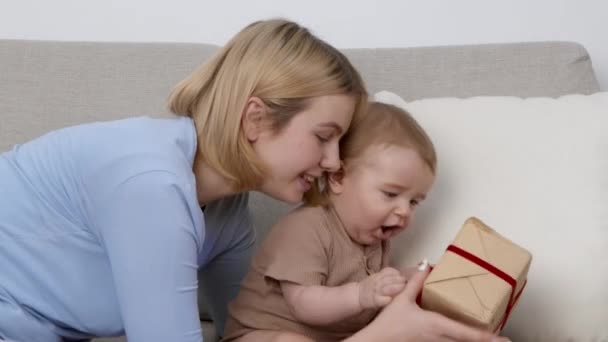 Mijn eerste vakantie. Schattige kleine baby krijgen geschenkdoos en onderzoeken, moeder genieten van het thuis, zijaanzicht — Stockvideo