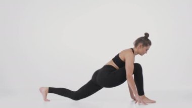 Esneme alıştırması. Beyaz stüdyo arka planında yoga egzersizi yapan esnek genç bir kadının yan görünümü.