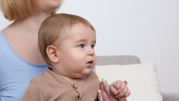 Η έννοια της βρεφικής ηλικίας. Κοντινό πορτρέτο του αξιολάτρευτου μωρού που κάθεται στα γόνατα της μητέρας και κοιτάζει στο σπίτι, κενό χώρο — Αρχείο Βίντεο
