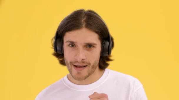Music lover. Young positive man wearing wireless headphones dancing, enjoying music, flirting to camera — Stock Video