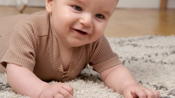 Šťastné dětství. Detailní záběr portrét rozkošného miminka ležícího na podlaze a usmívajícího se, odpočívajícího doma na koberci, prázdné místo — Stock video