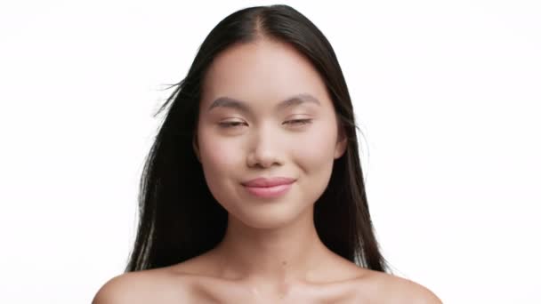 Fröhliche Asiatin mit fliegendem langen brünetten Haar, weißem Hintergrund — Stockvideo