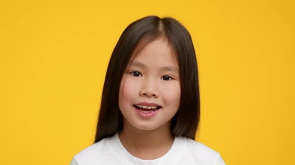 Портрет очаровательной азиатской дошкольницы, позирующей на жёлтом фоне — стоковое видео