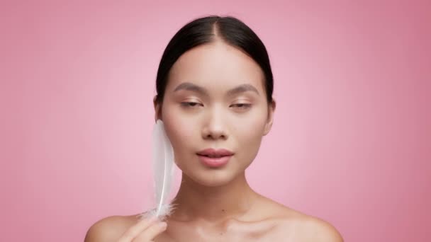 Korean Female Stroking Face With Feather Posing Over Pink Background — Stock Video