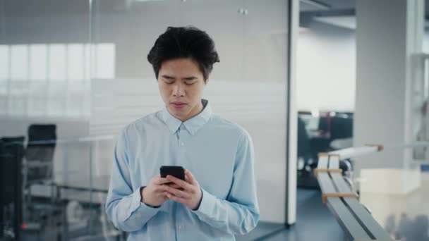Verärgerte asiatische Millennial Guy mit Telefon-SMS zu Fuß im Büro — Stockvideo