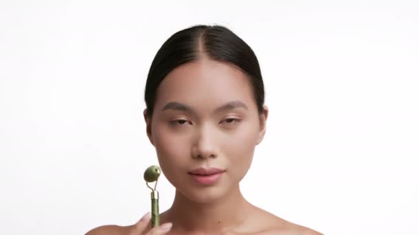 Senhora japonesa fazendo massagem facial com rolo sobre fundo branco — Vídeo de Stock