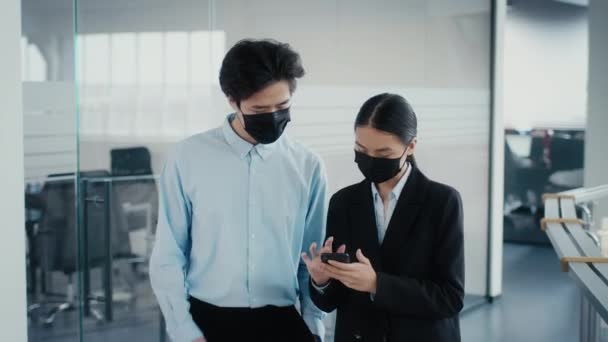 Chers collègues chinois utilisant un téléphone portable portant des masques faciaux marchant dans le bureau — Video