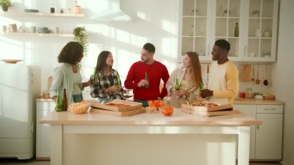 Концепция домашней вечеринки. Группа молодых счастливых многонациональных друзей, проводящих выходные вместе, звенящие бутылки с пивом — стоковое видео