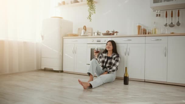 Propietario feliz. Joven mujer asiática alegre sentada en el suelo de la cocina con copa de vino, disfrutando de su propio apartamento — Vídeos de Stock
