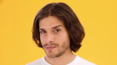 Erkek flörtü. Genç oyuncunun yakın portresi. Kaşlarını sallıyor, göz kırpıyor, kameraya kur yapıyor, sarı arka plan.