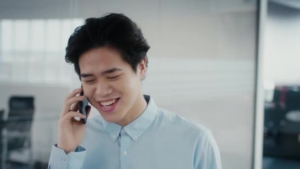 Gelukkig japans man praten op telefoon wandelen in modern kantoor — Stockvideo
