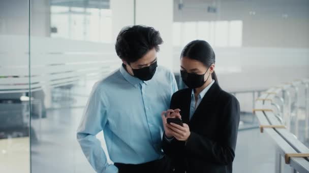 Deux collègues japonais utilisant des smartphones parlant portant des masques au bureau — Video