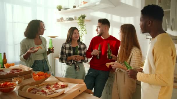 Jóvenes amigos diversos beber cerveza y comer pizza en casa, disfrutar de feliz fin de semana juntos en la cocina, zoom en tiro — Vídeo de stock