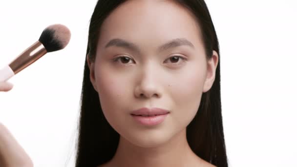 Mujer asiática haciendo maquillaje aplicando polvo con cepillo, fondo blanco — Vídeo de stock