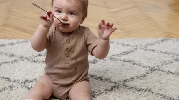 Miúdo a explorar o mundo. Adorável bebê brincando com colher de chá, sentado no tapete em casa, câmera lenta, espaço livre — Vídeo de Stock
