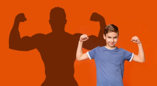 Sød dreng viser biceps på orange baggrund og bodybuilder form - Stock-foto