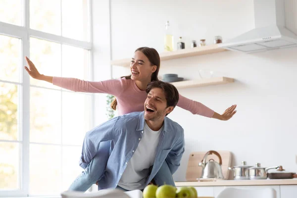 Cheerful excited positive caucasian young man with woman riding his back with arms to sides — Stock Photo, Image