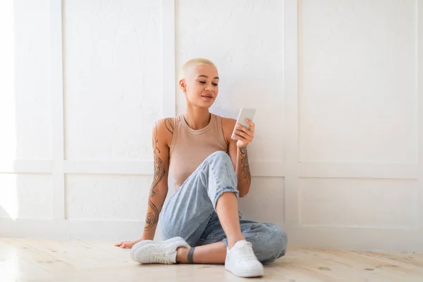 Fiatal elegáns hölgy ül a padlón okostelefonnal, dolgozik távolról vagy video chat ellen fehér fal, szabad hely — Stock Fotó